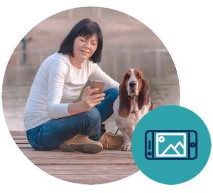 woman seated on dock with dog, looking at smartphone
